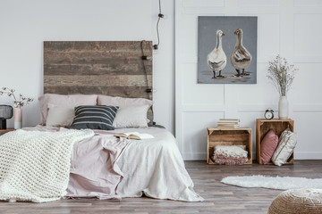 Spacious, feminine bedroom interior with rustic furniture, white walls, wooden crates and oil...