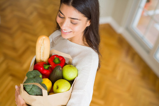 Beautiful young woman smiling holding a paper bag full of fresh groceries at home
