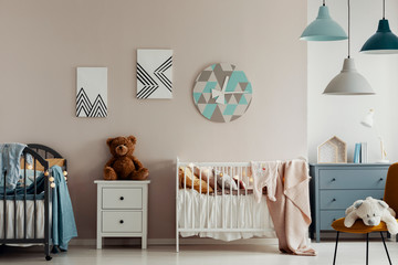A teddy bear, two beds and a large clock on a beige wall in bright and warm bedroom interior for...