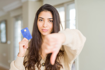 Young woman holding credit card as payment with angry face, negative sign showing dislike with...