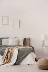 Stylish white lamp on simple nightstand table next to warm bed with cozy grey bedding