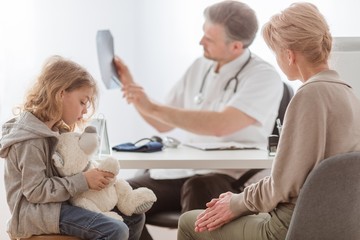 Mom and cute sick son in front of the handsome pediatrician's desk