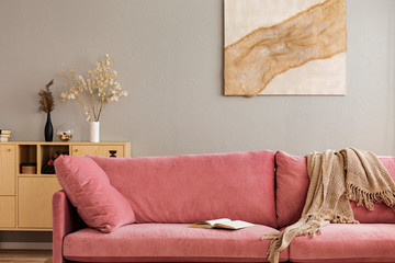 Comfortable velvet pastel pink couch in elegant beige interior with abstract painting