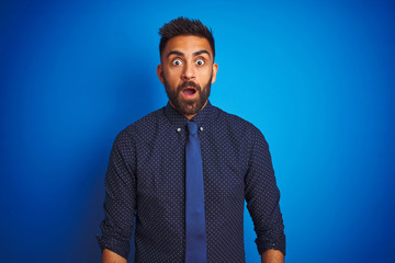 Young indian businessman wearing elegant shirt and tie standing over isolated blue background...
