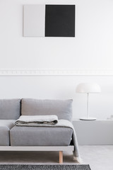Trendy living room interior with white wall, painting and grey settee