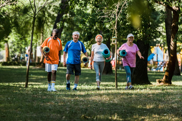 Obraz premium selective focus of cheerful multicultural and senior pensioners walking with fitness mats in park