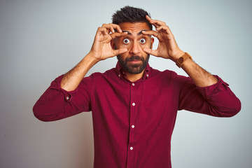 Young indian man wearing red elegant shirt standing over isolated grey background Trying to open...