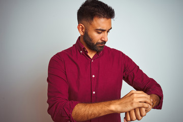 Young indian man wearing red elegant shirt standing over isolated grey background Checking the time on wrist watch, relaxed and confident