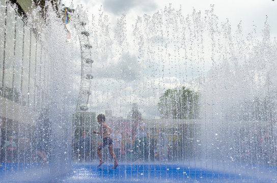 Young Boy Playing Inside A Fountain In The Summer Heatwave In London, England