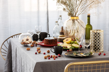 Stylish chair next to dining table with food, fruits and flowers
