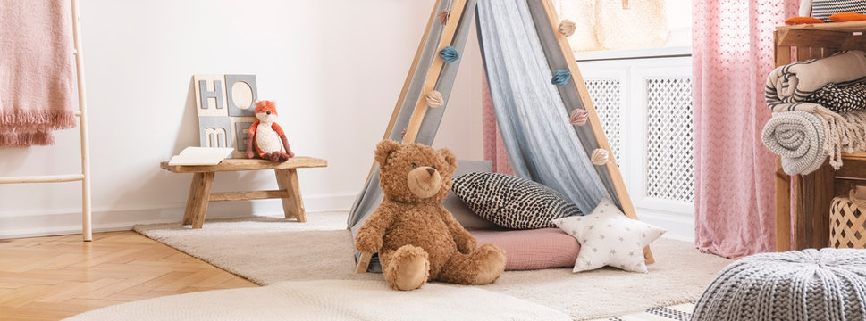Cute teddy bear in pink and blue colored kids room in stylish modern apartment, real photo