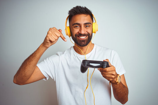 Arab indian gamer man playing video game using headphones over isolated white background very happy pointing with hand and finger