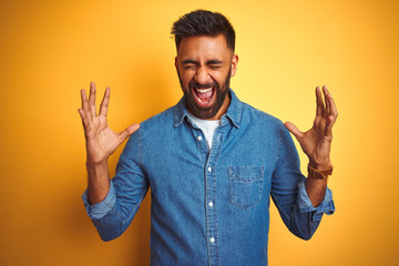 Young indian man wearing denim shirt standing over isolated yellow background celebrating mad and...