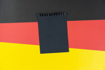 Fototapeta premium Blacklist Germany. Mourning, ban, sanctions, politics. black sheet of notebook lies on German flag. Mock up, copy space, pattern, cardboard texture.