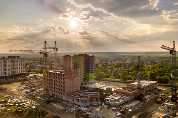 Fototapeta premium Aerial view of building site. Apartment or office building under construction. Tower cranes on suburb landscape and blue sky copy space background.
