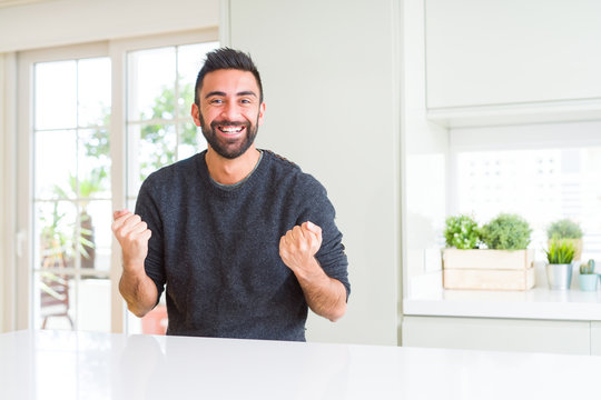 Handsome hispanic man wearing casual sweater at home celebrating surprised and amazed for success with arms raised and open eyes. Winner concept.