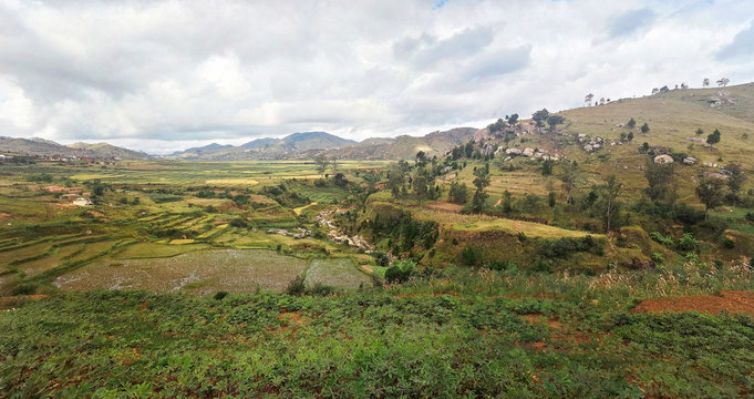 Typical Madagascar landscape in region near Ambositra small hills covered with green grass and bushes, red clay houses and wet rice fields near.