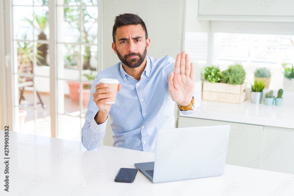 Poster Handsome hispanic man working using computer laptop and drinking a cup of coffee with open hand doing stop sign with serious and confident expression, defense gesture