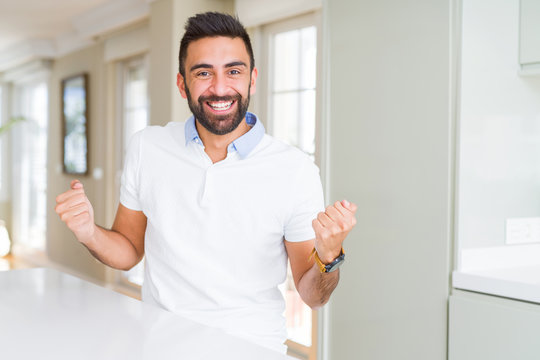 Handsome hispanic man casual white t-shirt at home celebrating surprised and amazed for success with arms raised and open eyes. Winner concept.