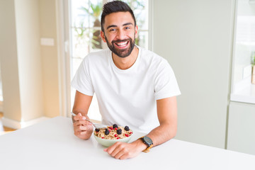 Handsome hispanic man eating healthy breakfast in the morning at home with a happy face standing and smiling with a confident smile showing teeth