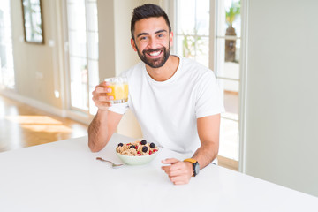 Handsome man smiling eating healthy breakfast and drinking orange juice in the morning