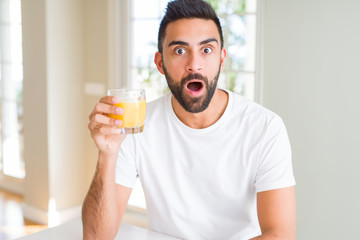 Handsome hispanic man drinking healthy orange juice scared in shock with a surprise face, afraid and excited with fear expression