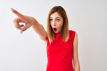 Redhead businesswoman wearing elegant red dress standing over isolated white background Pointing with finger surprised ahead, open mouth amazed expression, something on the front