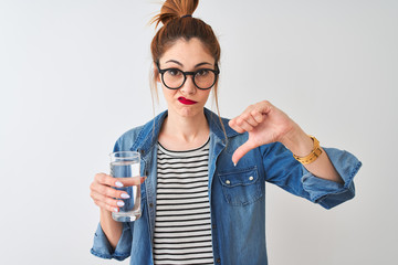 Young beautiful redhead woman drinking glass of water over isolated white background with angry face, negative sign showing dislike with thumbs down, rejection concept