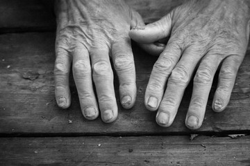 Black and white photo of old sick male hands on an antique rough wooden surface, concept of pleading and asking for help