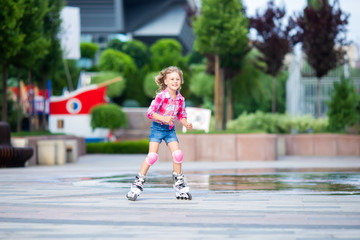 Little pretty girl on roller skates at a park. Cheerful preschool girl wearing inline roller skates...