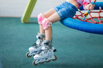 Close up photo of little girl's legs on roller skates at a park. Cheerful preschool girl wearing...