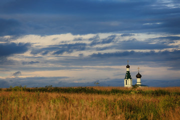 Fototapeta premium Beautiful landscape in Russia. Orthodox temple in the field and blue clouds in the evening sky