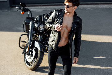 Fototapeta na wymiar full length view of handsome young man with muscular torso in leather jacket looking away and smoking cigarette