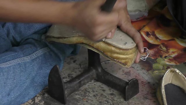 A cobbler repairing the shoe with nails and hammer