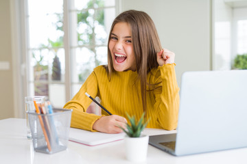 Beautiful young girl studying using computer laptop and writing on notebook screaming proud and celebrating victory and success very excited, cheering emotion