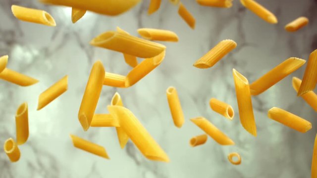 Pasta Penne flyi in the air on a white marble background in slow motion