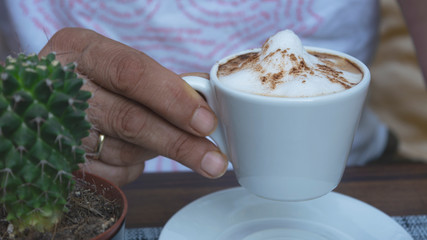 Close up of middle aged man holding a cup of coffee in a modern cafeteria. 