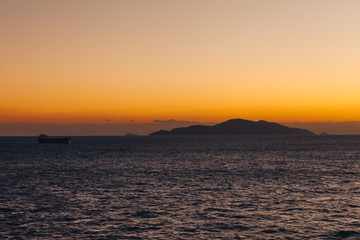 Ship sailing at sunset with island silhouette background and orange sky