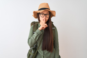 Chinese hiker woman wearing canteen hat glasses backpack over isolated white background asking to be quiet with finger on lips. Silence and secret concept.