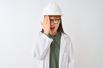 Young chinese engineer woman wearing coat helmet glasses over isolated white background covering one eye with hand, confident smile on face and surprise emotion.