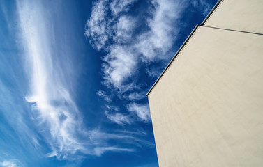 Large flat wall of a modern building without windows against a blue sky with white clouds