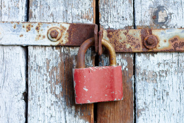 Old brown padlock on a gray door with wooden planks of cracked paint and rust. Vintage gates with metal stripes and bolts