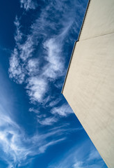 Large flat wall of a modern building without windows against a blue sky with white clouds