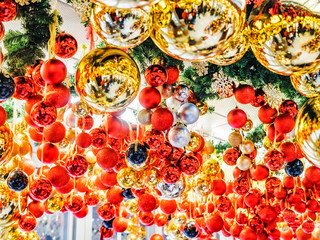 Fototapeta na wymiar Many large golden balls with festooned fir tree garlands and red ribbons are hung indoors. New Year and Christmas tree decorations. Beautiful Christmas background. Street decorations in Europe