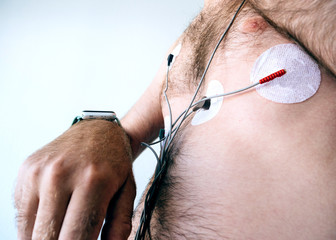 Side view of man setting smartwatch wearing a heart monitor holter attached to sensors stuck to chest designed to be worn for 24 hours and monitor heart activity during this period to indicate any