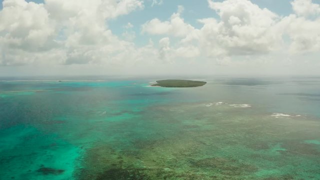Tropical island in the blue water of the sea and the atoll against the sky and clouds, aerial view. Daco Island, Siargao. Summer and travel vacation concept
