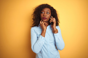 Young african american woman talking on the smartphone over isolated yellow background serious face...