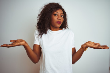 Young african american woman wearing t-shirt standing over isolated white background clueless and...