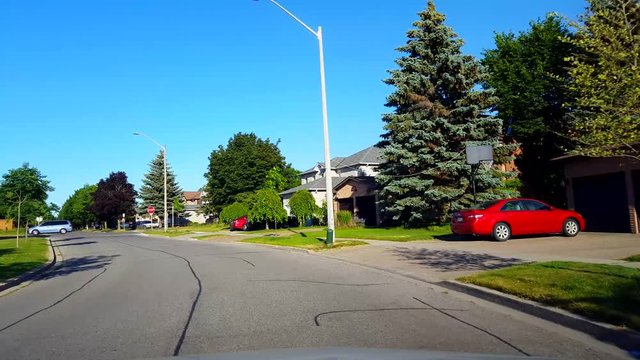 Driving Around a Bend of Residential City Road With Lush Trees During Summer Day.  Driver Point of View POV Turning Along Beautiful Sunny Suburban Street.
