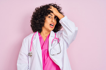 Young arab doctor woman with curly hair wearing stethoscope over isolated pink background surprised...